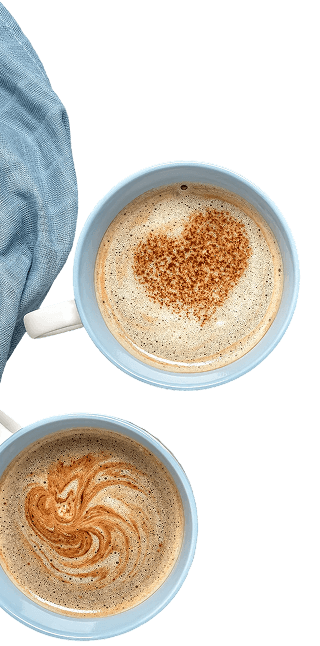 Zwei Kaffeetassen mit Latte-Art: eine mit Herzmuster, die andere mit wirbelnden Brauntönen, auf einem blauen Tuch.