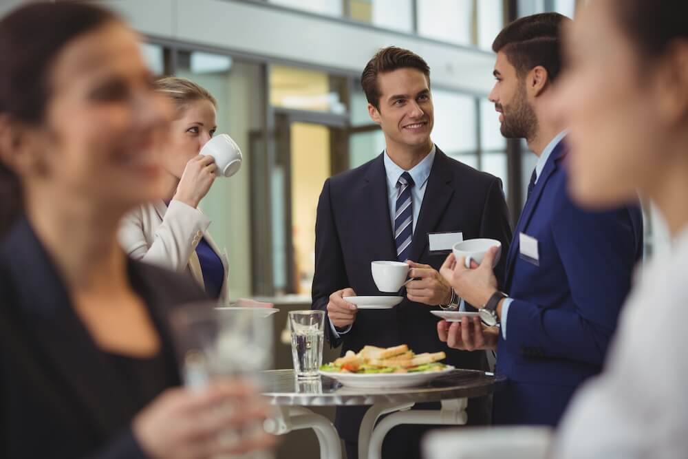Geschäftliches Networking: Personen in Anzügen unterhalten sich bei einem Buffet, Getränke und Snacks auf dem Tisch.