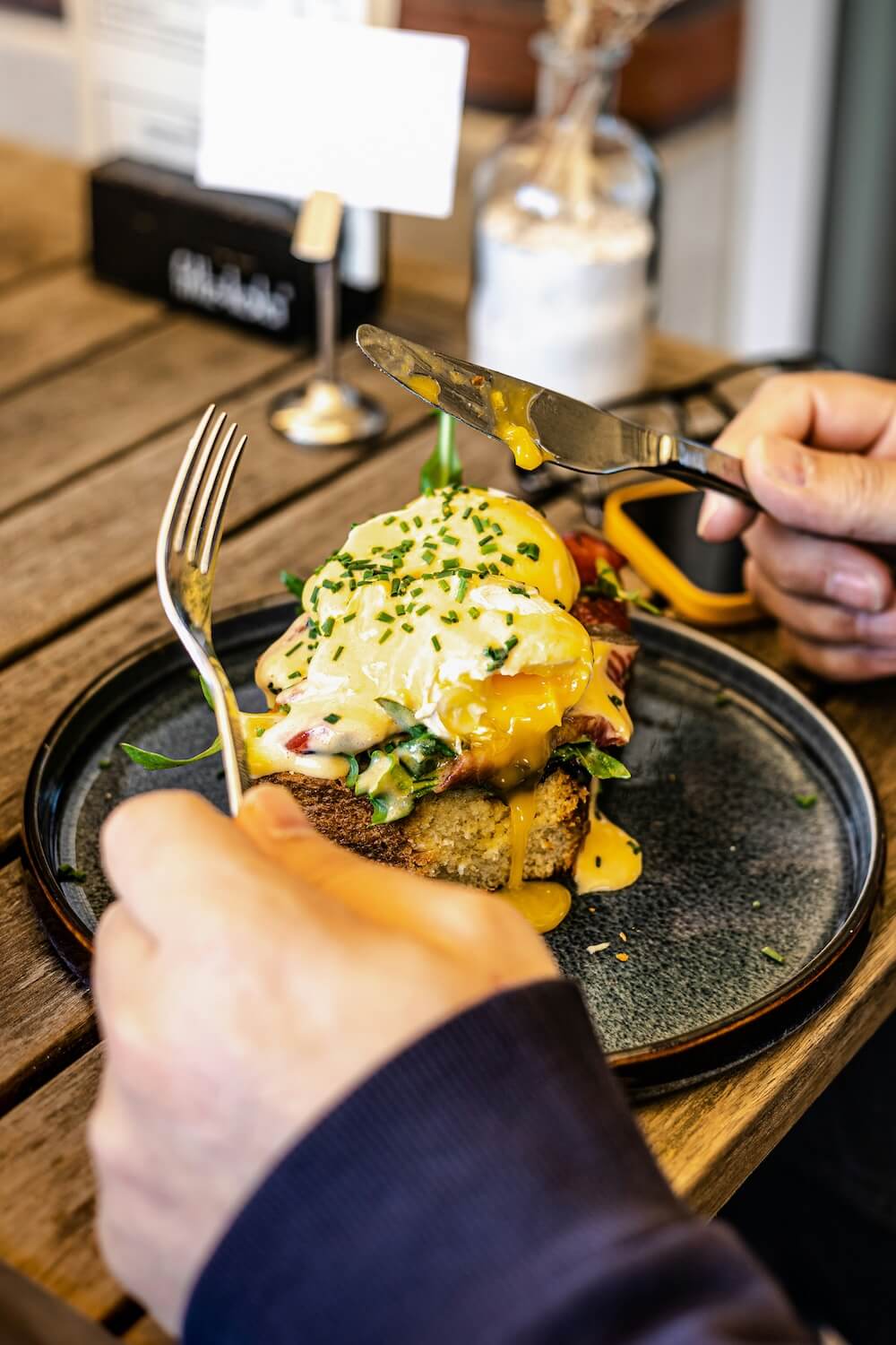 Eine Person schneidet ein Gericht mit pochiertem Ei, Spinat und Sauce Hollandaise auf einem Teller.