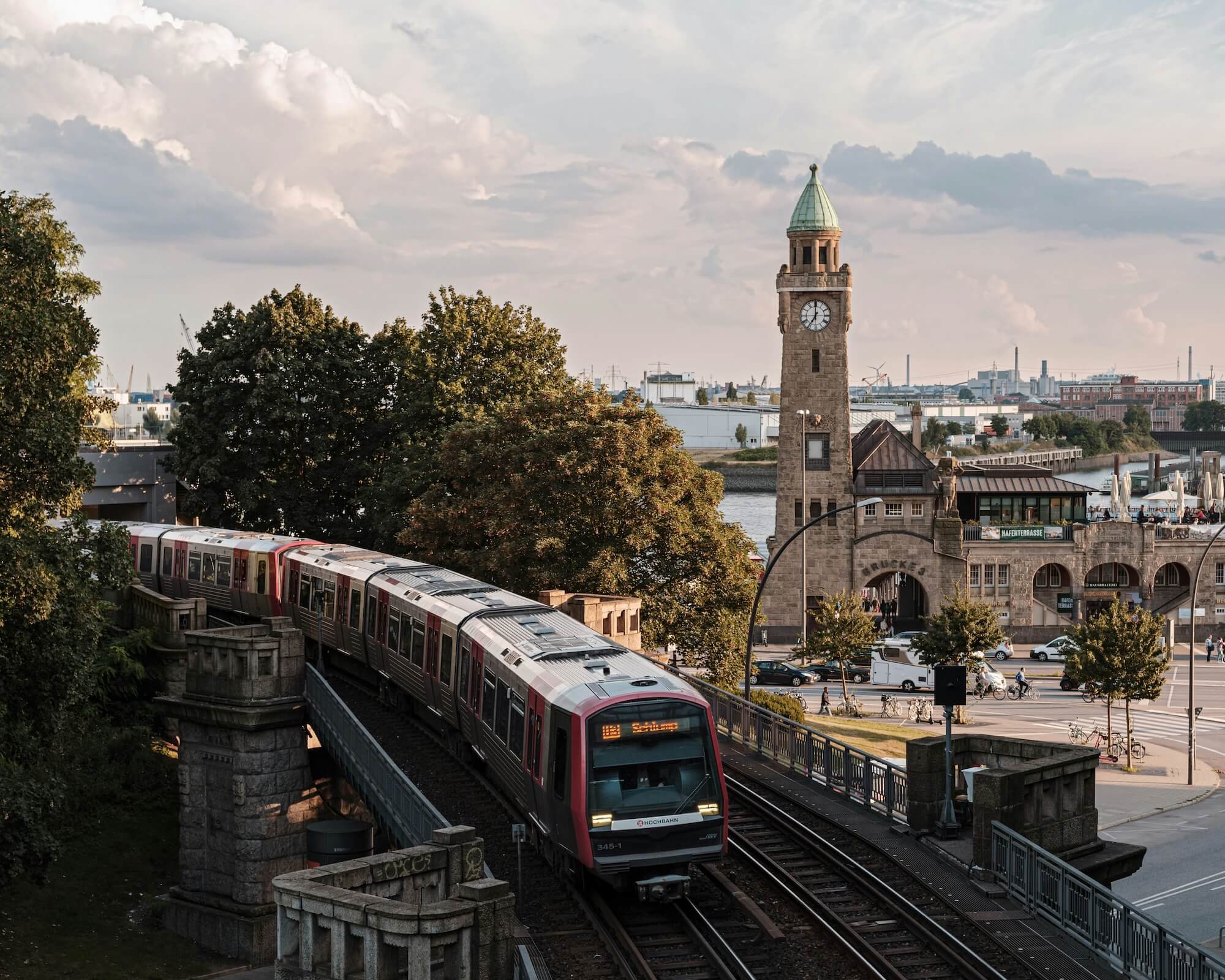 Ein Zug fährt über eine Brücke, im Hintergrund ist ein historischer Uhrturm und der Hafen sichtbar.