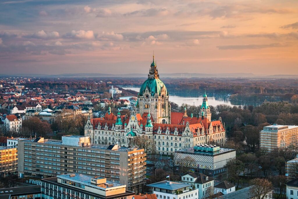 Panoramablick auf das Neue Rathaus in Hannover bei Sonnenuntergang, umgeben von Stadtlandschaft und Wasser.