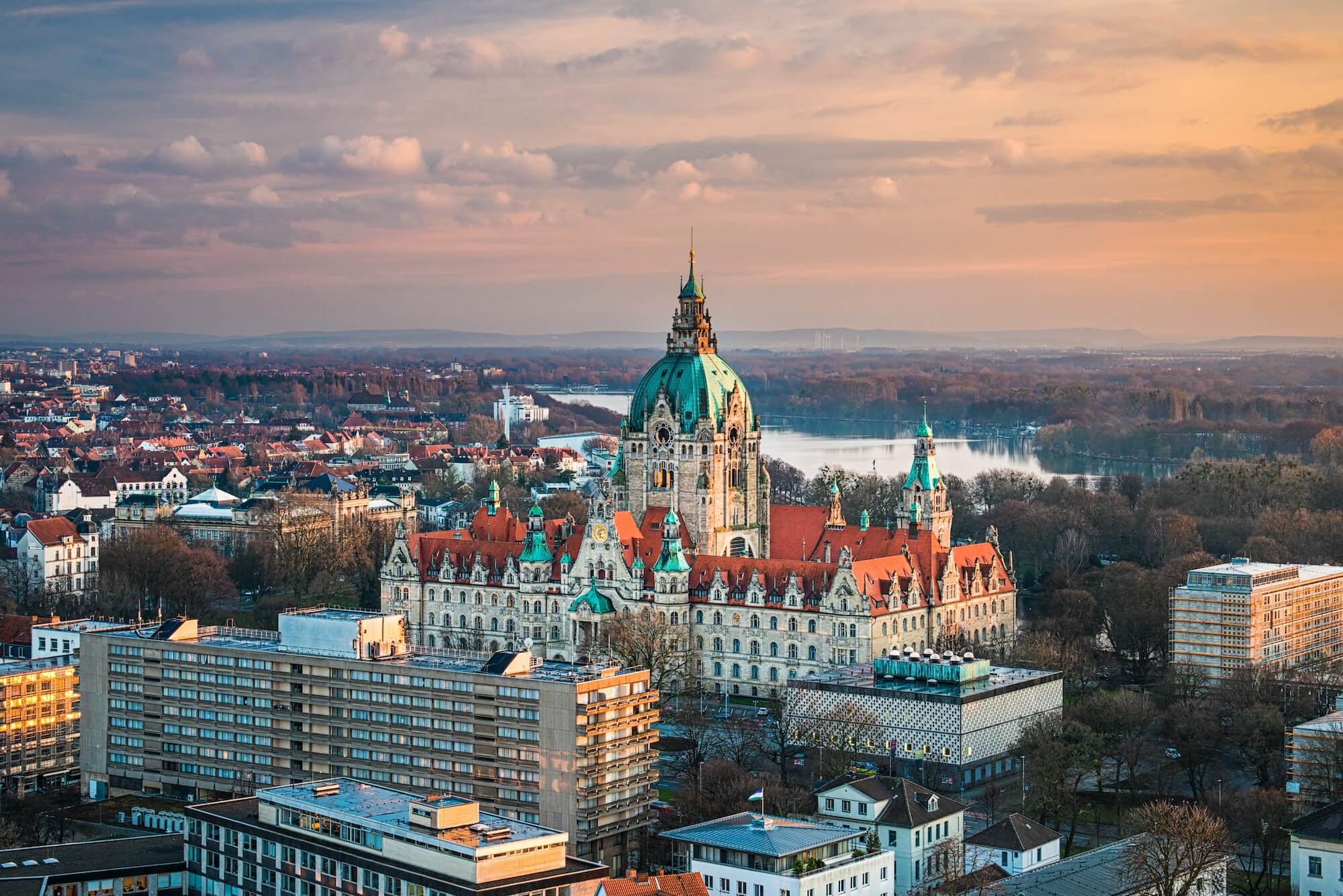 Panoramablick auf das Neue Rathaus in Hannover bei Sonnenuntergang, umgeben von Stadtlandschaft und Wasser.