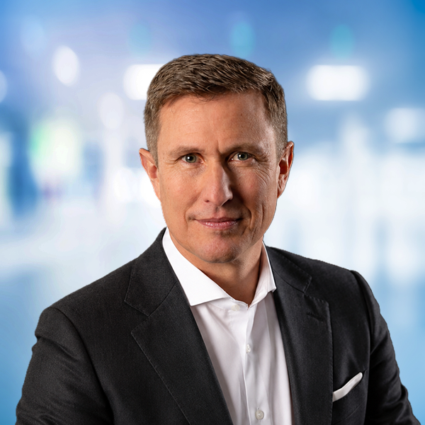 Mann in Anzug mit kurzem, gestyltem Haar, neutralem Hintergrund und fokussiertem Blick.