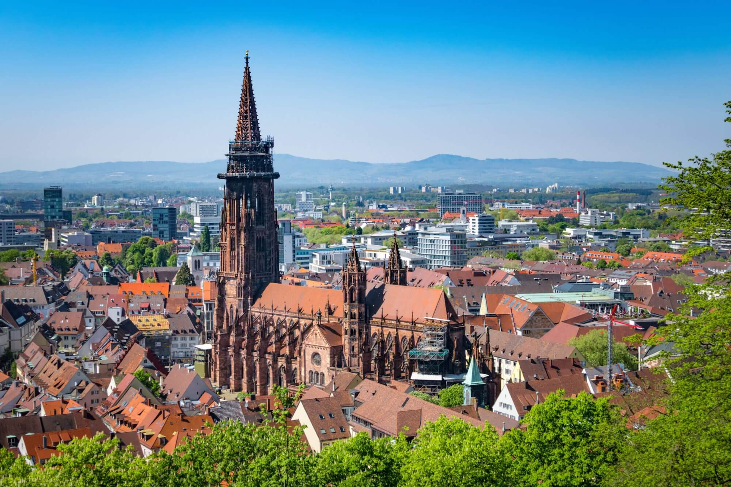 Blick auf Freiburg mit dem imposanten Münster und roten Dächern, umgeben von moderner Architektur und grünen Hügeln.
