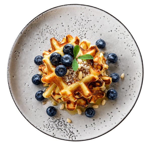 Gestapelte Waffeln mit Blaubeeren und Honig auf einem hellen, gesprenkelten Keramikteller.