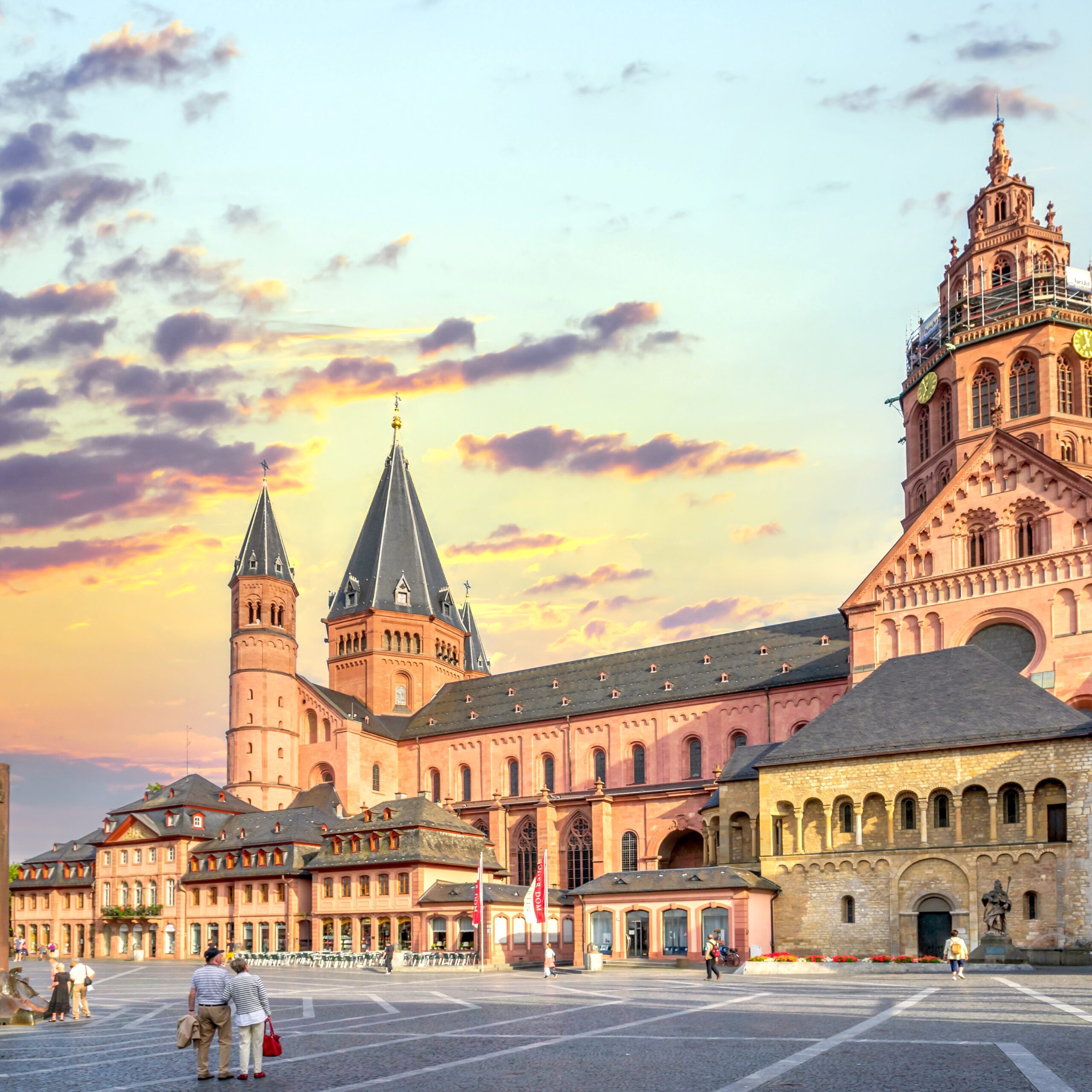Der Dom von Mainz mit seinen markanten T&uuml;rmen, umgeben von einem Platz und einem farbenfrohen Abendhimmel.